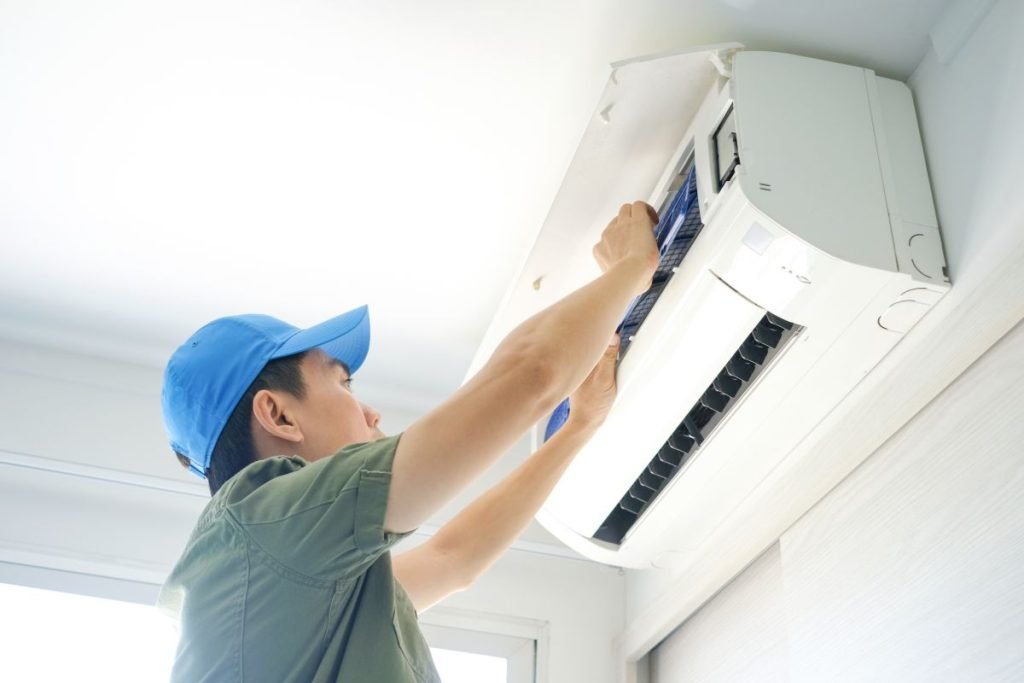 A man wearing a blue hat is repairing an air conditioner, focused on the task at hand.
