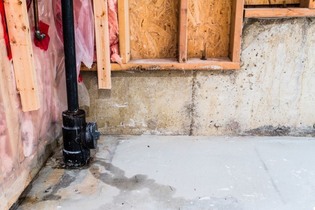 A room featuring a visible water pipe and a wall made of drywall, showcasing a simple interior design.