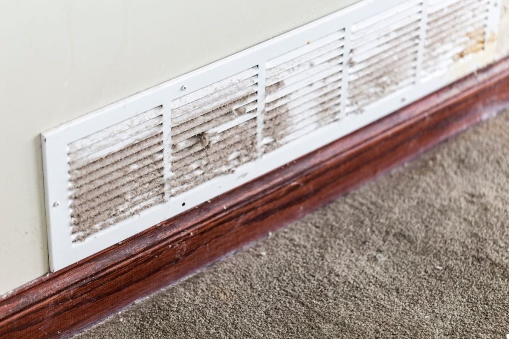 A close-up of a dirty air vent covered in mold, highlighting poor air quality in the room.